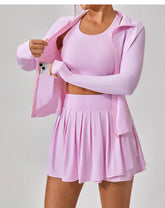 Woman wearing light pink athleisure set with pleated skirt, fitted crop top, and zip-up jacket