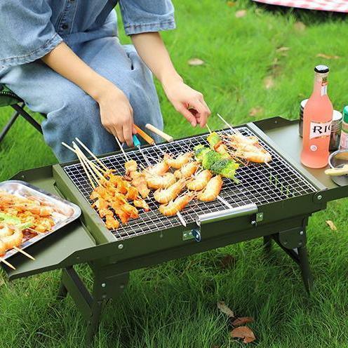 Person in light blue denim jumpsuit with relaxed fit, sitting outdoors grilling skewers.
