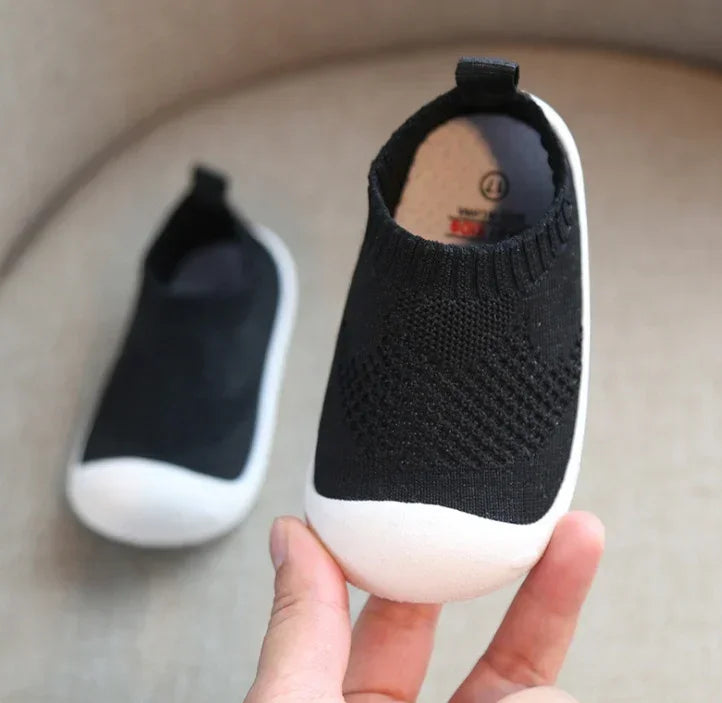 Black slip-on knit sneaker with white rubber toe, soft flexible material, casual fit.
