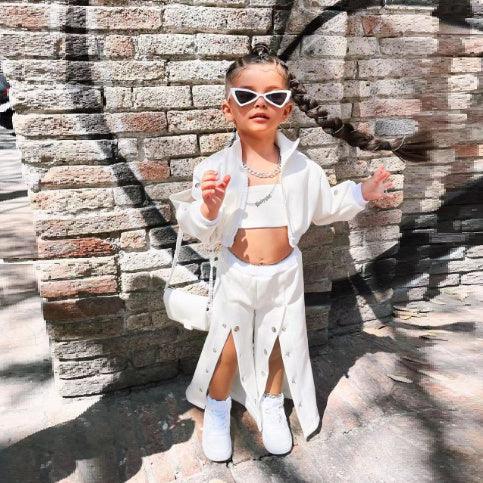 Child wearing white crop top and jacket, skirt with front slits, white sneakers, and sunglasses, streetwear style