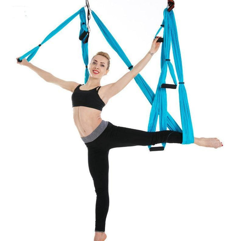 Woman in black athletic crop top and leggings doing aerial yoga with blue hammock, slim fit activewear.