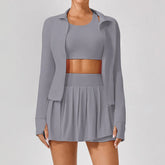 Woman wearing a light gray athletic set with cropped jacket, sports bra, and pleated mini skirt