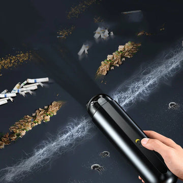 Handheld black vacuum cleaner removing dust, crumbs, and debris from a dark surface.