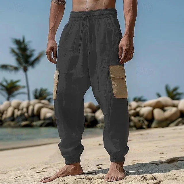 Man wearing loose fit black cargo joggers with beige pockets on a beach