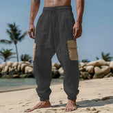 Man wearing loose fit black cargo joggers with beige pockets on a beach