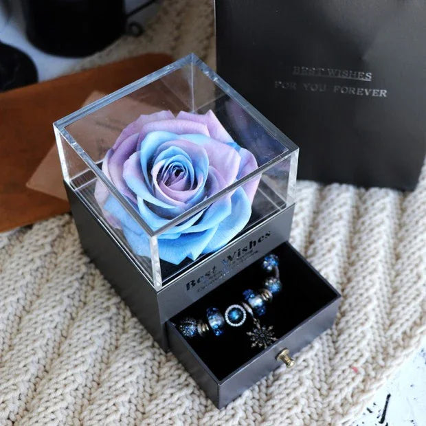 Pastel blue and purple rose in clear display box with drawer containing blue charm bracelet