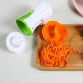 Handheld spiral vegetable slicer with green accent, spiralized carrot on cutting board