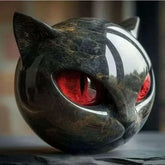 Glossy black marble cat sculpture with red eyes and rounded features on dark background.