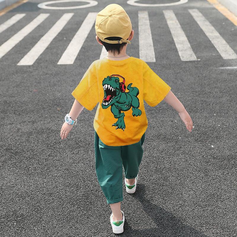 Kid in loose yellow dinosaur graphic t-shirt, green pants, and cap walking outdoors