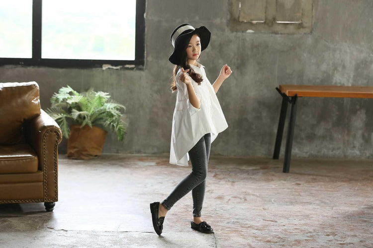 Girl in oversized white shirt, black wide-brim hat, grey skinny jeans, and black loafers