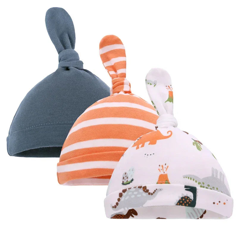 Set of three soft cotton baby hats with knot top in blue, orange stripes, and dinosaur print.