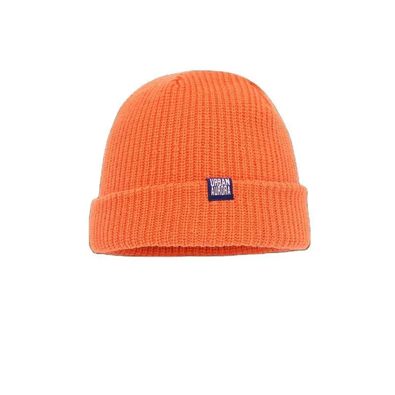 Bright orange ribbed knit beanie hat with fold-up cuff and small front patch, casual streetwear style