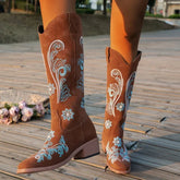 Brown suede knee-high western boots with blue floral embroidery, classic fit, outdoor setting