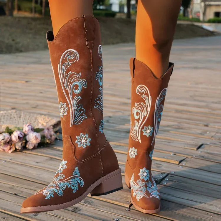 Brown suede knee-high western boots with blue floral embroidery, classic fit, outdoor setting