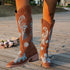 Brown suede knee-high western boots with blue floral embroidery, classic fit, outdoor setting