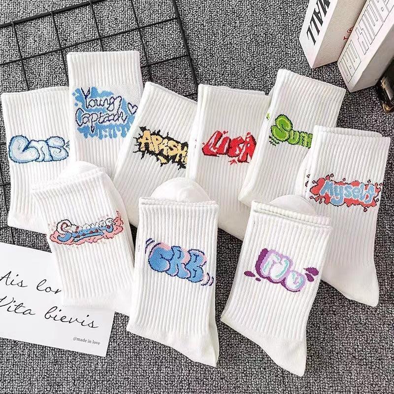 Assorted white ribbed crew socks with colorful graffiti text designs on a gray surface