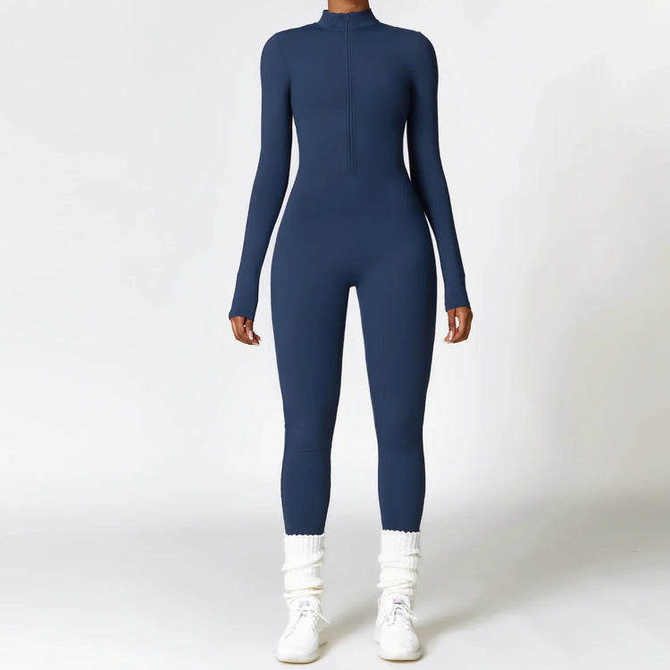 Woman wearing navy blue fitted long sleeve jumpsuit with zip front, white sneakers, and cozy socks