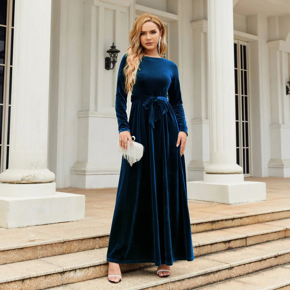 Woman in a long sleeve navy blue velvet maxi dress with waist tie, standing outdoors