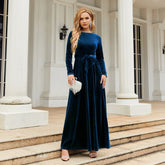 Woman in a long sleeve navy blue velvet maxi dress with waist tie, standing outdoors