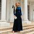 Woman in a long sleeve navy blue velvet maxi dress with waist tie, standing outdoors