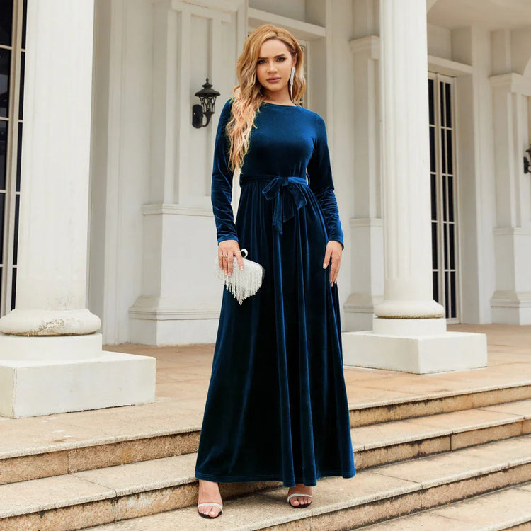 Woman in a long sleeve navy blue velvet maxi dress with waist tie, standing outdoors