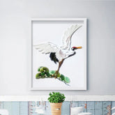 Framed artwork of a white crane with black wingtips above green leaves on a white wall