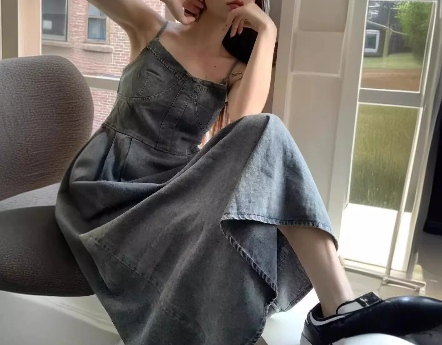 Woman wearing a grey denim sleeveless dress with a relaxed fit, sitting indoors.