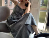 Woman wearing a grey denim sleeveless dress with a relaxed fit, sitting indoors.