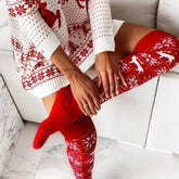Woman wearing cozy white and red knit sweater dress with matching over-the-knee socks featuring snowflake and reindeer patterns