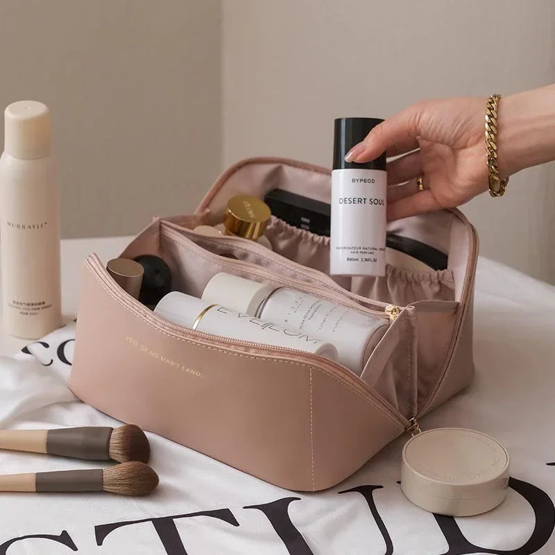 Beige makeup bag with a gold zipper, holding assorted beauty products and brushes, soft material, roomy fit.