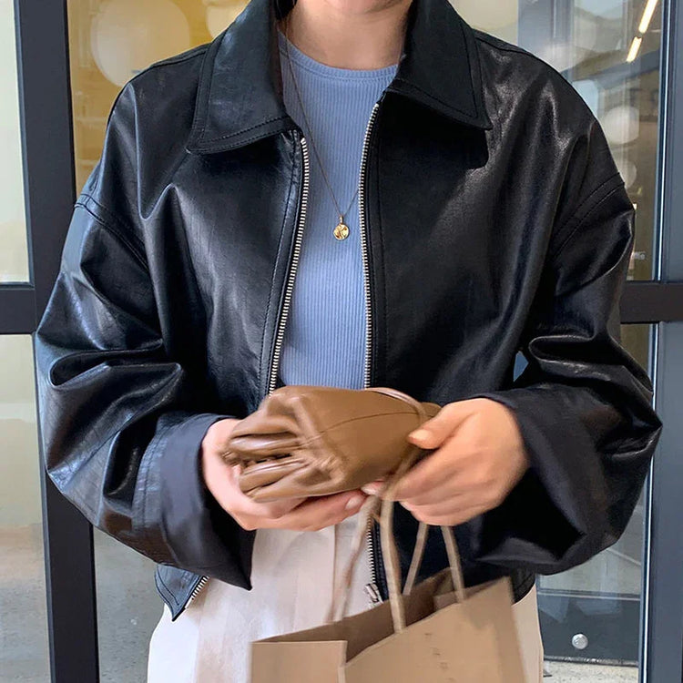 Woman wearing a black faux leather jacket with relaxed fit, blue ribbed top, and white pants