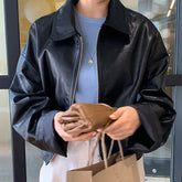 Woman wearing black faux leather jacket with relaxed fit and light blue ribbed top