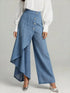 Woman wearing wide-leg blue denim pants with asymmetric wrap detail and a white blouse