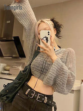 Woman wearing a loose knit gray cropped sweater, high-waisted black pants, and double belt