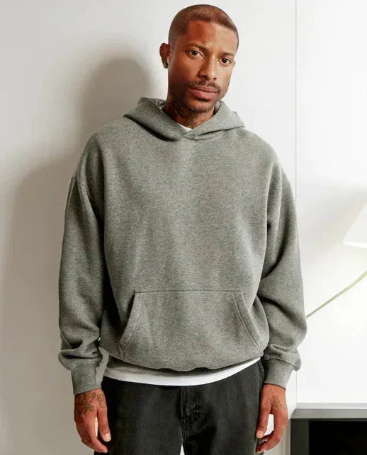 Man wearing a loose fit grey hooded sweatshirt with kangaroo pocket and black pants