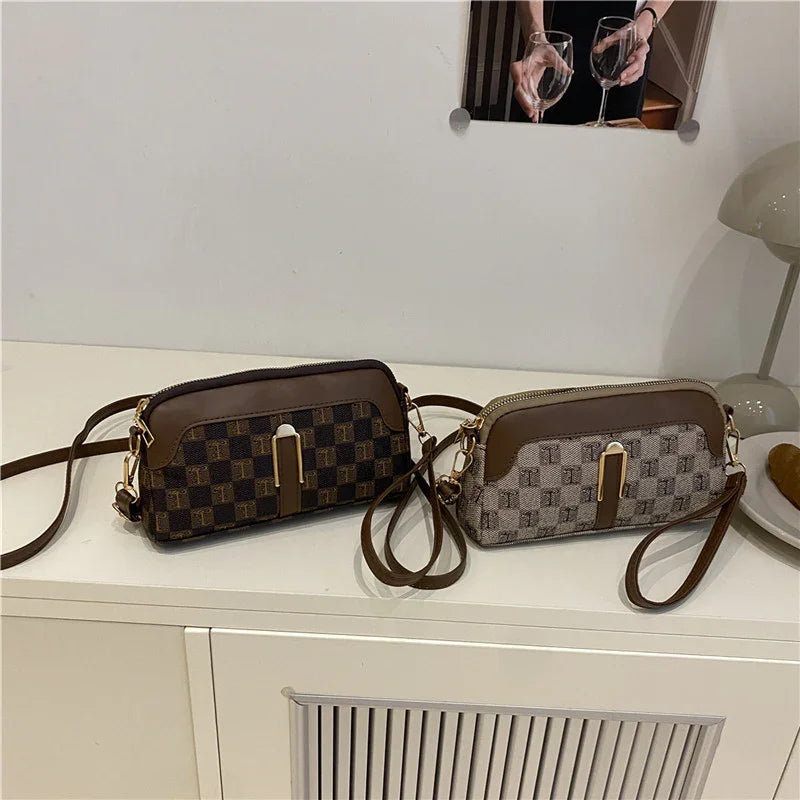 Two checkered shoulder bags with brown leather accents and gold hardware on a white table