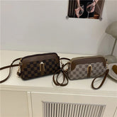 Two checkered shoulder bags with brown leather accents and gold hardware on a white table