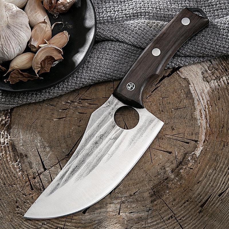 Stainless steel chef knife with dark wood handle on rustic wooden surface, next to garlic cloves.