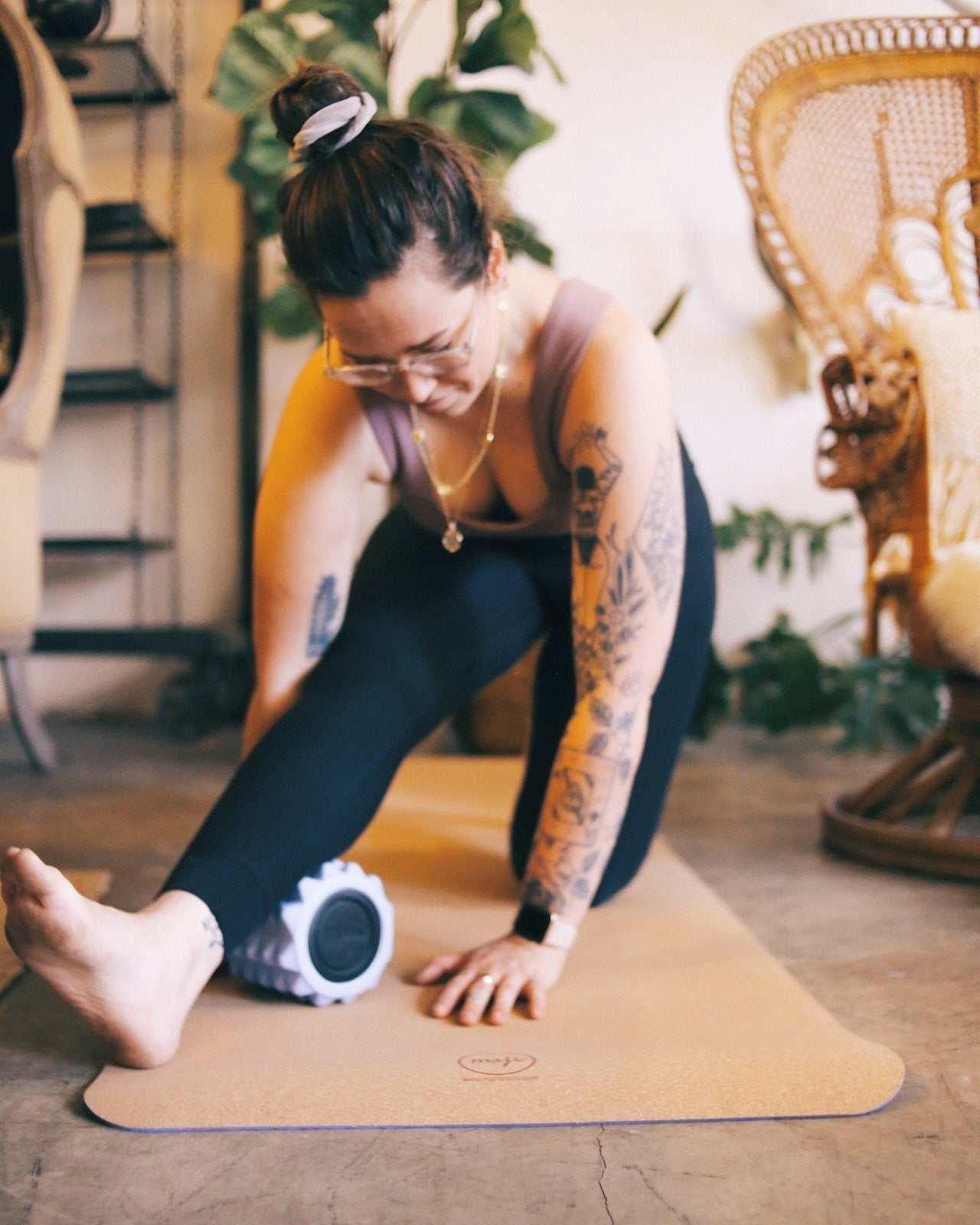 Woman in fitted black leggings and mauve tank top stretching on a yoga mat indoors