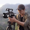 Man outdoors using KOMERY RX100 4K digital video camera with tripod, capturing 4K Ultra HD video and 48MP photos in scenic landscape setting