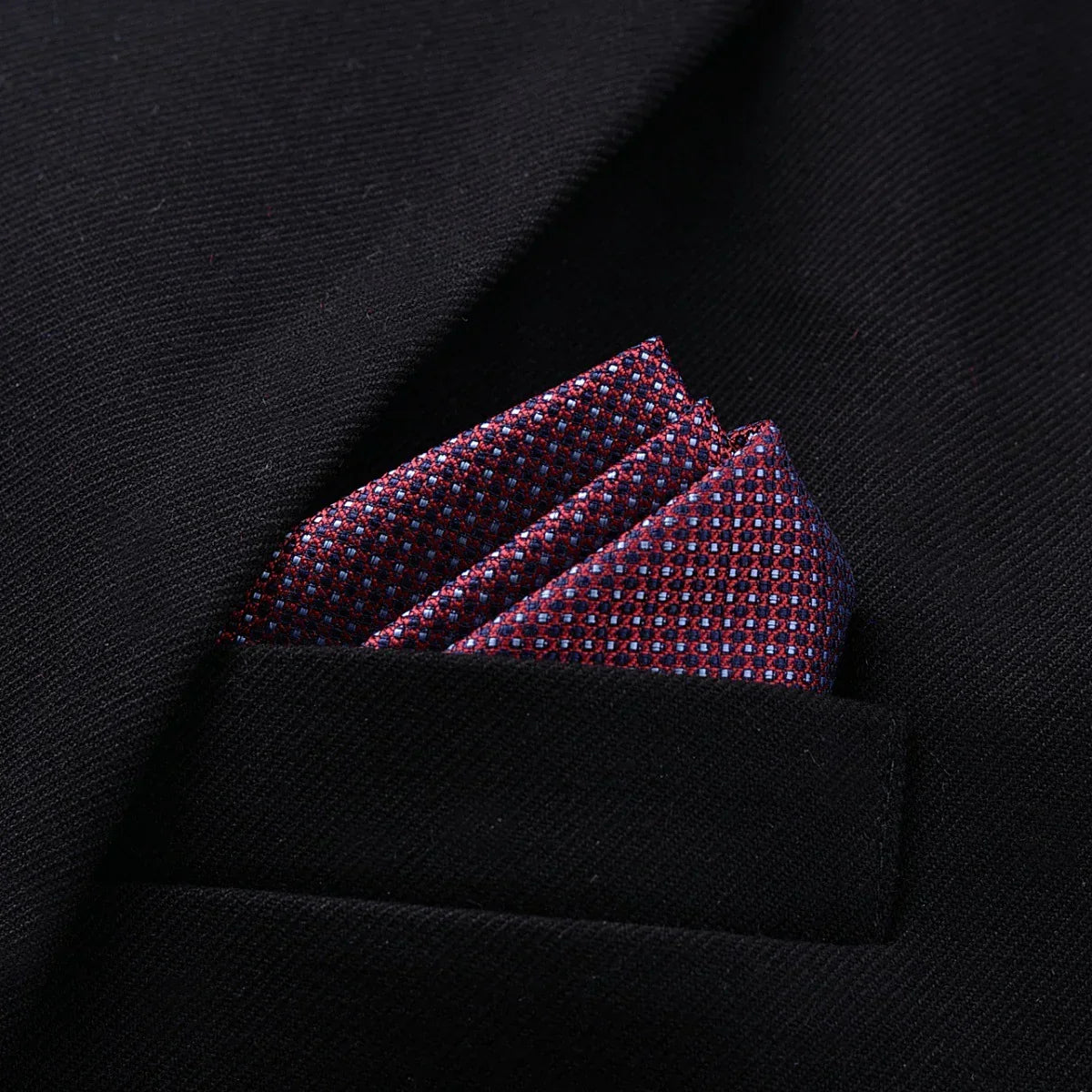 Red and blue patterned pocket square in black textured suit jacket, modern slim fit style.