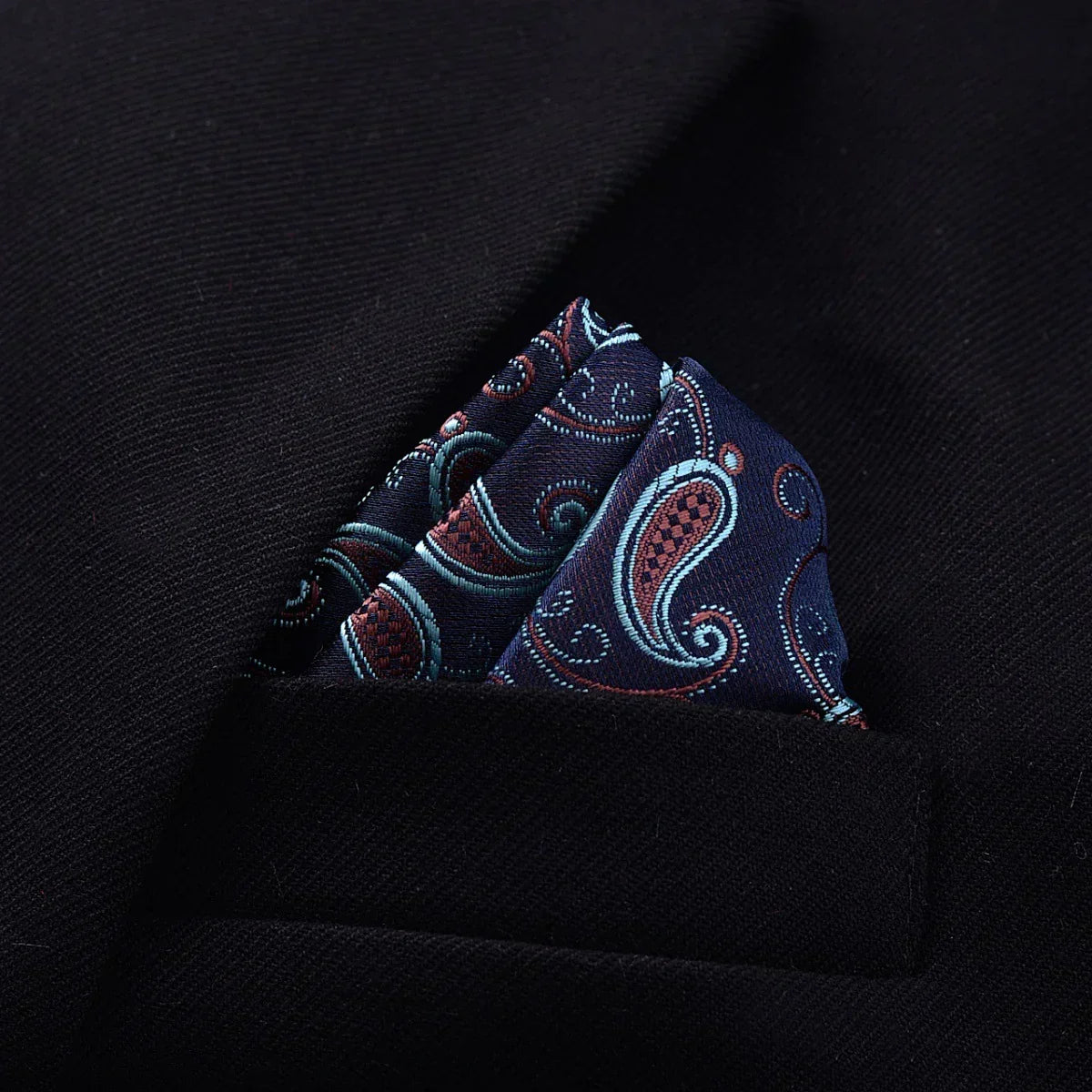 Navy blue paisley silk pocket square in a black suit jacket pocket, classic fit style.