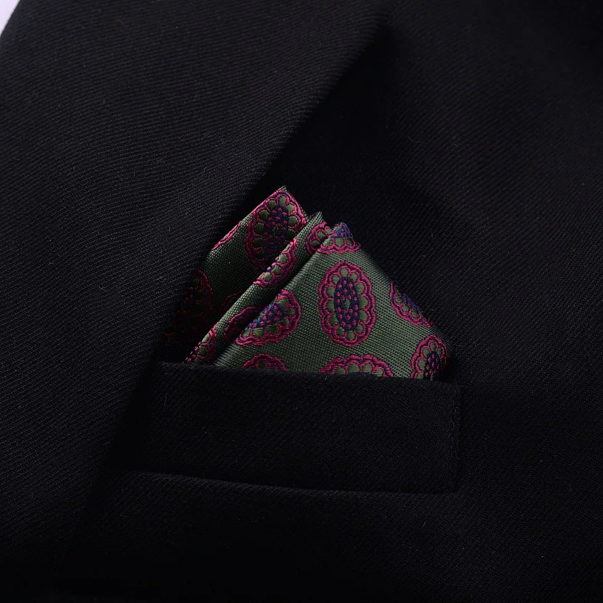 Green patterned silk pocket square in black suit jacket pocket, modern formal style