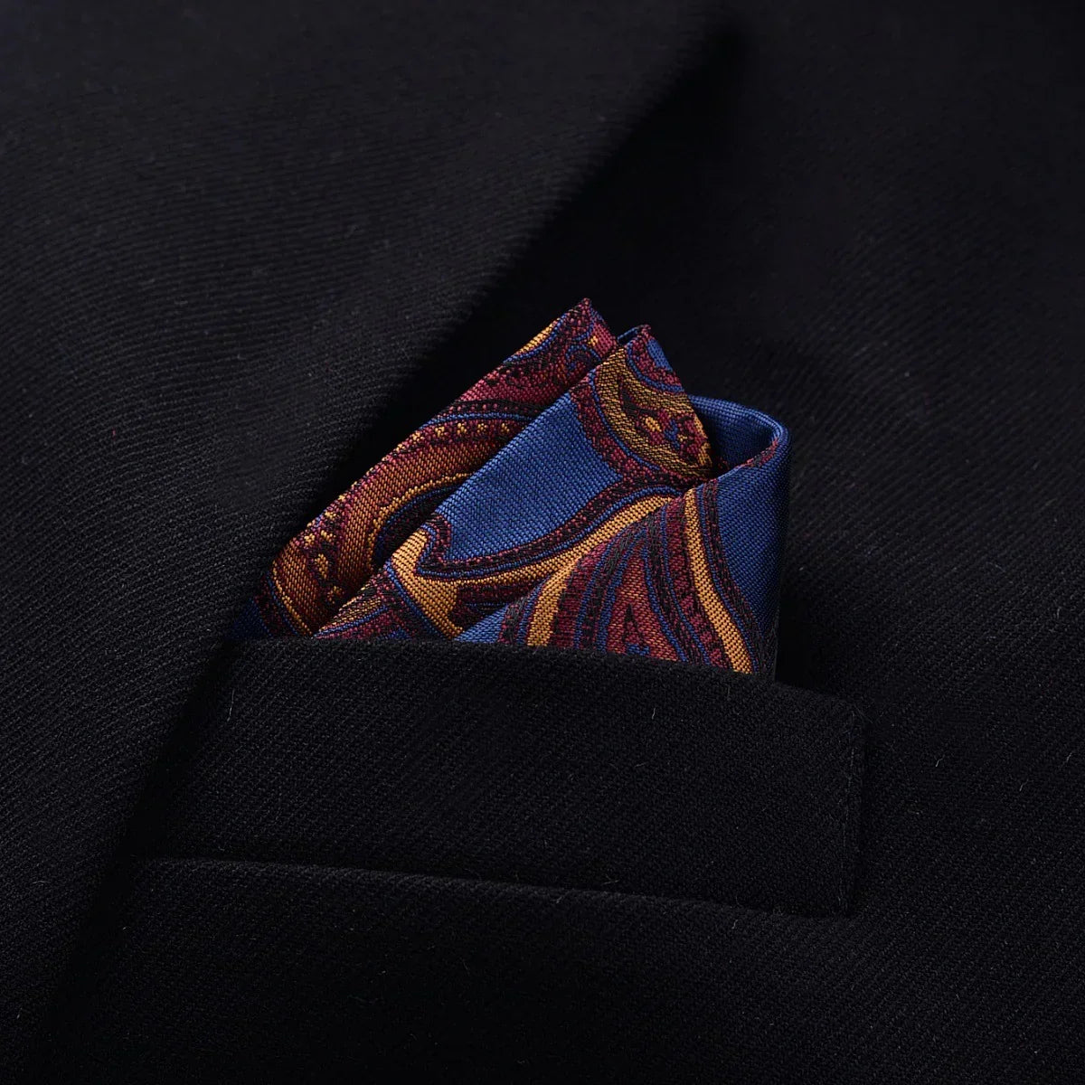 Navy blue suit with a paisley silk pocket square in blue, gold, and maroon tones.