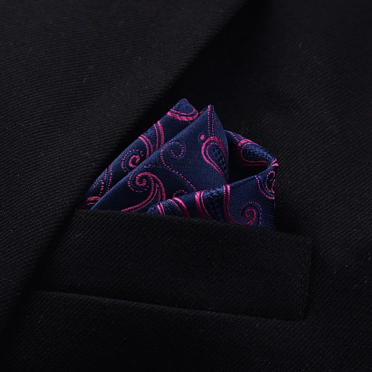 Navy blue paisley silk pocket square with pink accents styled in a black blazer pocket
