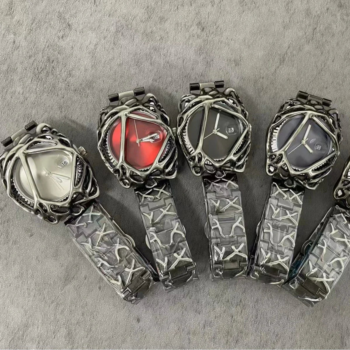 Futuristic silver metal watches with abstract case design, grey and red dials, and patterned bands.