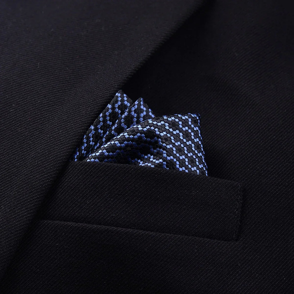 Black blazer with textured blue patterned pocket square, close-up on chest pocket