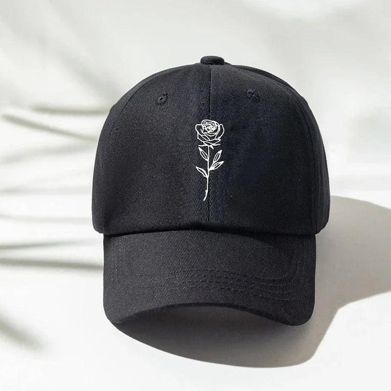 Black cotton dad cap with white embroidered rose design, curved brim, minimalist streetwear style