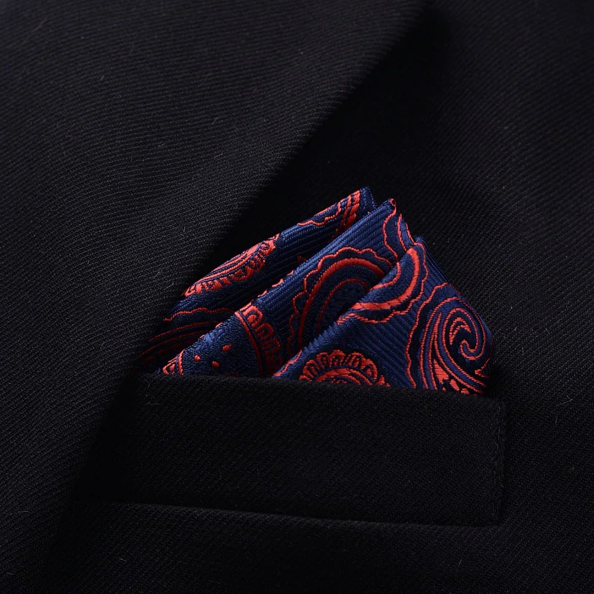 Navy blue paisley pocket square with red accents in a black blazer pocket