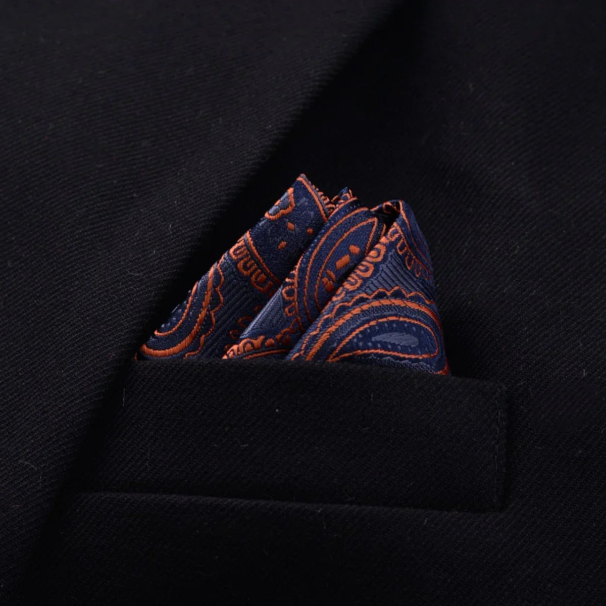 Navy and orange paisley silk pocket square in black suit jacket pocket, close-up